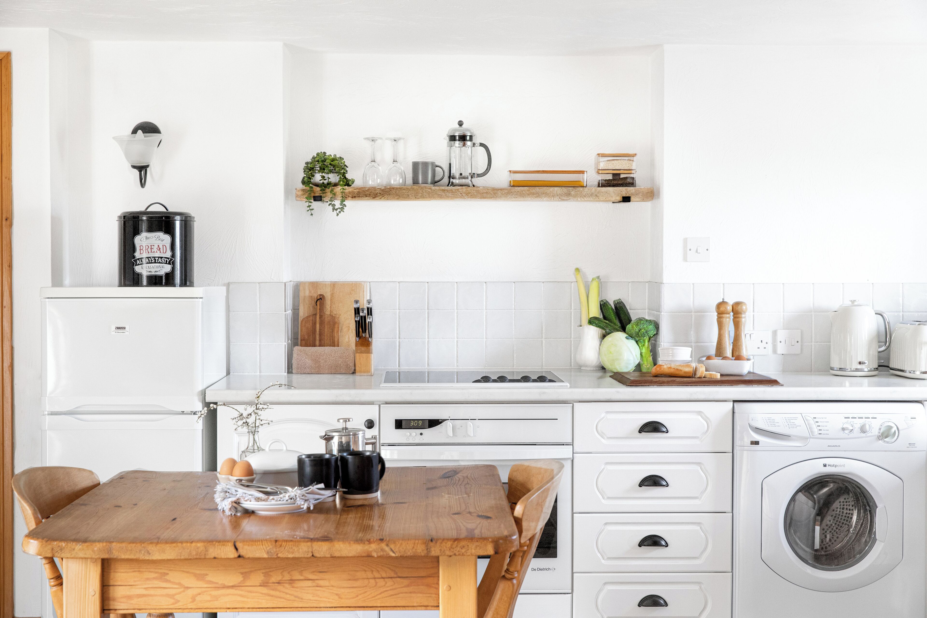 A modern kitchen with white appliances, a wooden table, and a built-in washing machine.