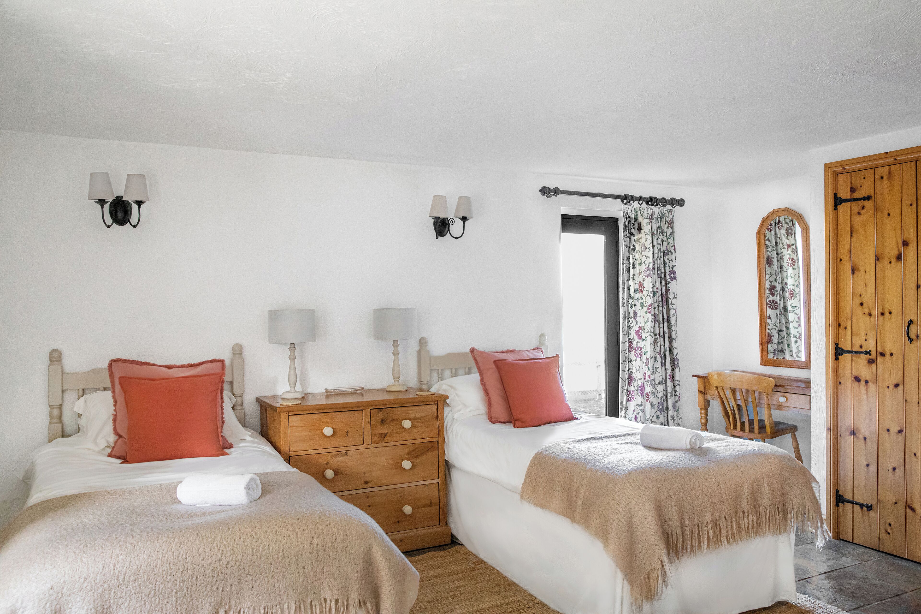 A bedroom with two beds, a wooden dresser, a mirror, and a wooden wardrobe.