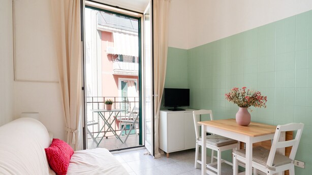 A bedroom with a bed, a desk with a TV, a small table with chairs, and a balcony with a view of buildings. - Rifugio Pugliese by Wonderful Italy (Bari)