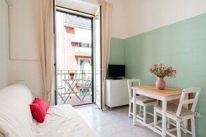 Una camera da letto con un letto, una scrivania con televisore, un tavolino con sedie e un balcone con vista sugli edifici.