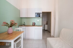 Una cucina compatta con mobili bianchi, un piano di lavoro in legno e un vaso rosa con fiori.