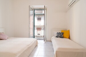 Una camera da letto con due letti, una finestra e una porta aperta su un balcone.