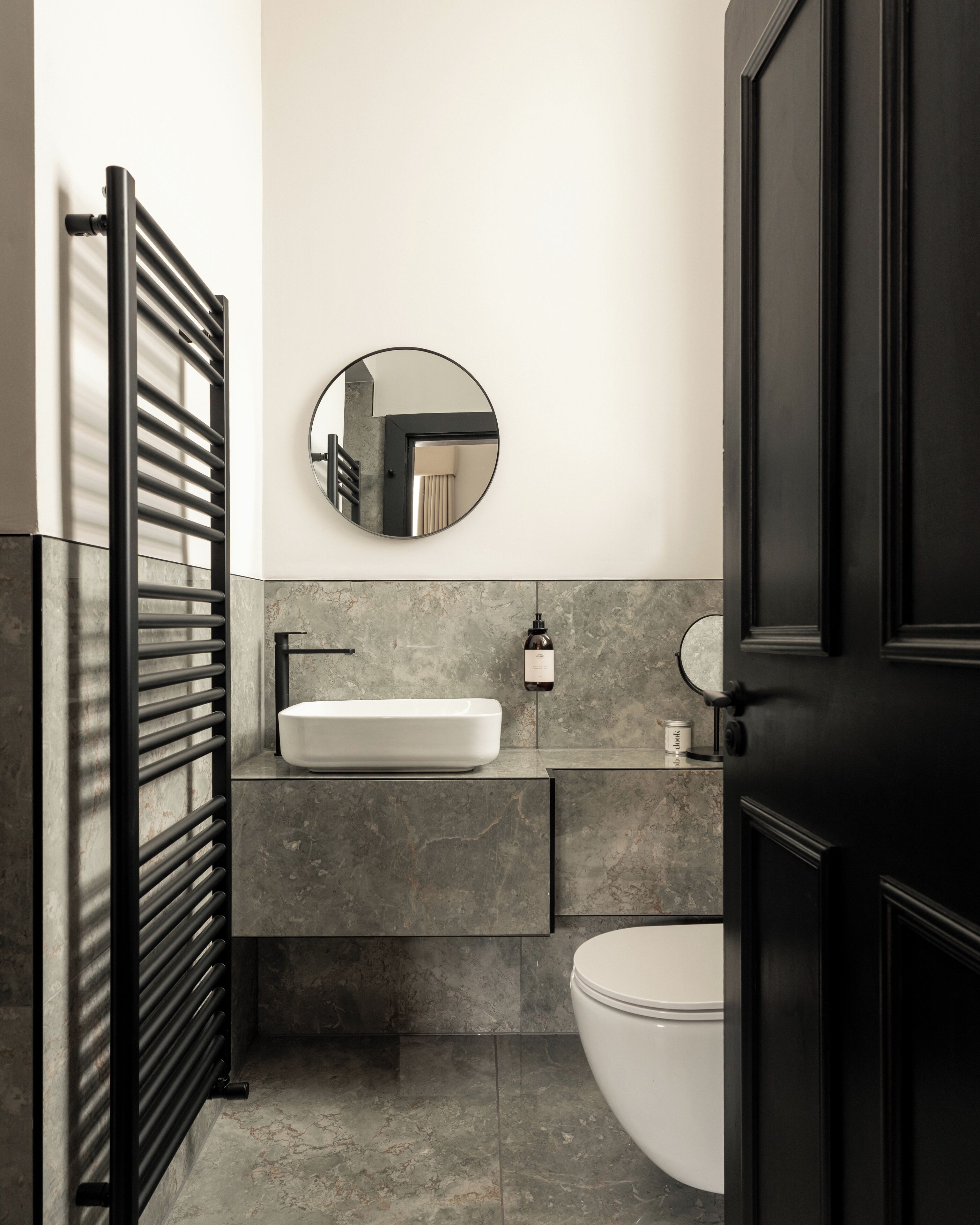 A modern bathroom with a black door, a white sink, a round mirror, and a toilet.