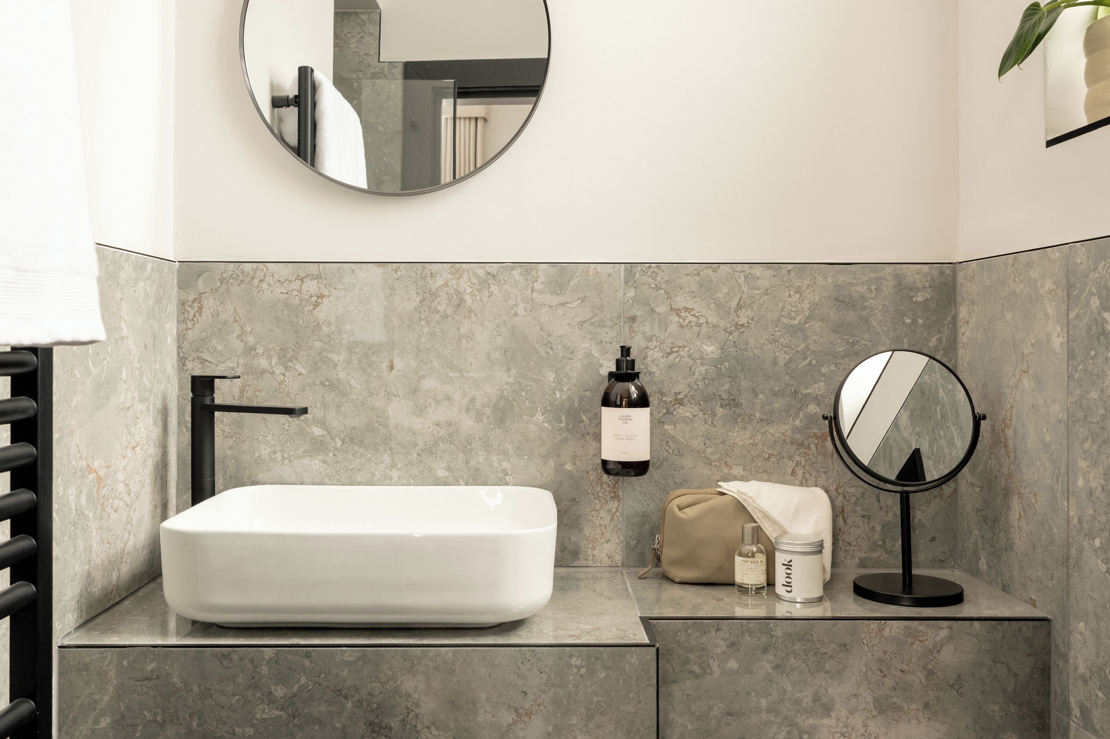 A bathroom with a rectangular white sink, a black faucet, a round mirror, and a beige towel on the counter.