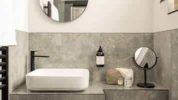 A bathroom with a rectangular white sink, a black faucet, a round mirror, and a beige towel on the counter.