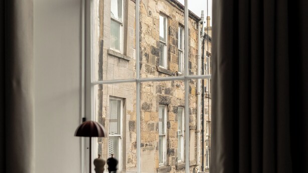 A room with a large window, a table with a lamp, and a chair. - Moment Blythswood Street (Glasgow)