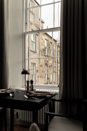 A room with a large window, a table with a lamp, and a chair. - Moment Blythswood Street (Glasgow)
