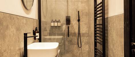 Un baño moderno con ducha envuelta en vidrio, lavabo blanco y toallero negro.