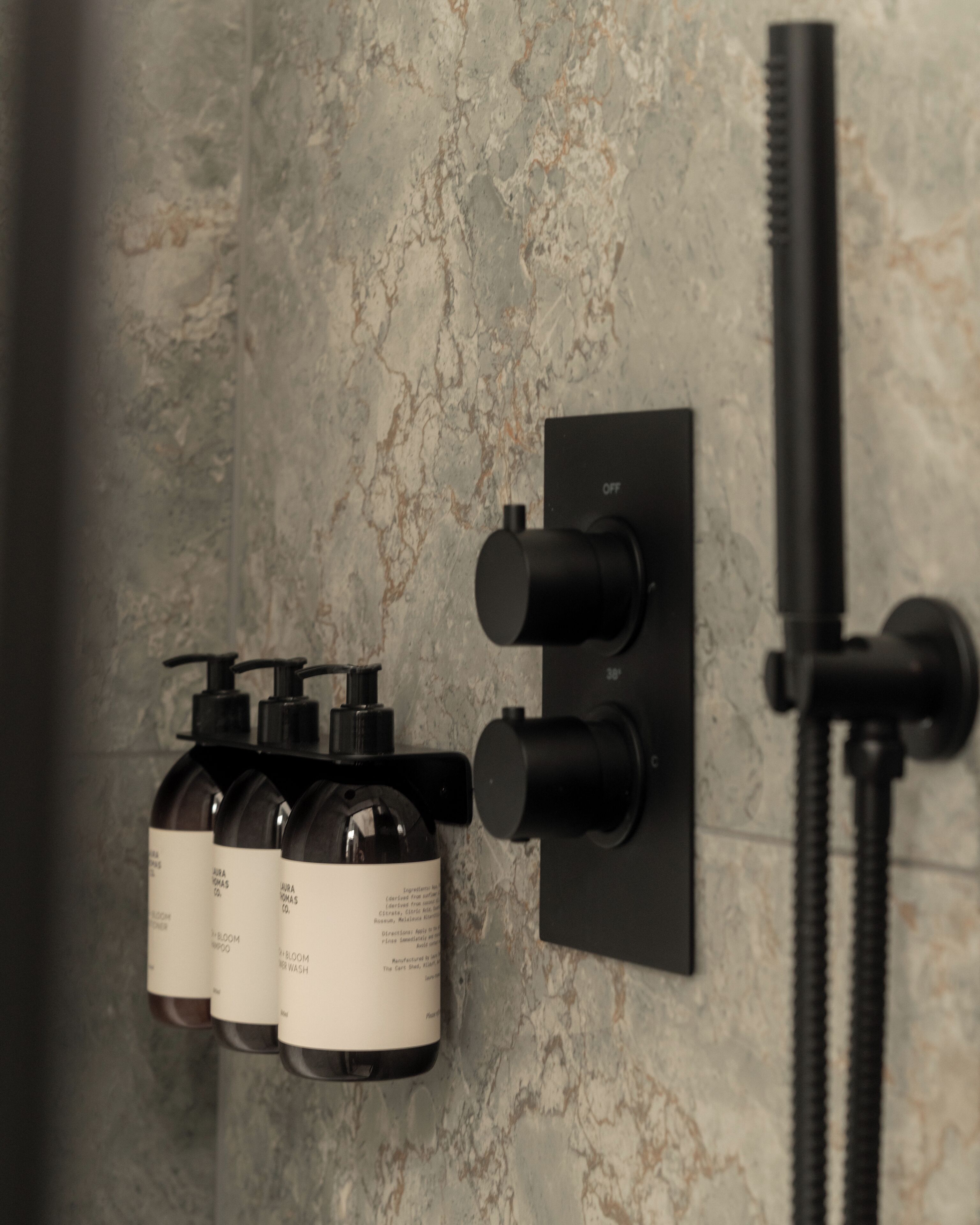 A bathroom with a marble wall, a black faucet, and three bottles of shampoo.