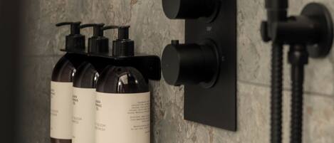 A bathroom with a marble wall, a black faucet, and three bottles of shampoo.