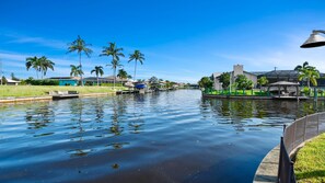 A calm canal with a row of houses and palm trees on one side and a gazebo on the other. - Love Bird Canalfront Villa Lounge Terrace Heated Pool pet Friendly (Cape Coral)