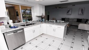 A modern kitchen with white cabinets, a double sink, and a dishwasher. There is a dining area with a sofa and a coffee table. - Love Bird Canalfront Villa Lounge Terrace Heated Pool pet Friendly (Cape Coral)