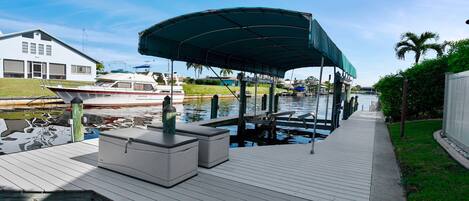 A dock with a covered seating area, a boat, and a house in the background.