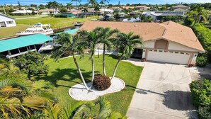 A residential property with a swimming pool, a boat docked nearby, and a well-maintained lawn with palm trees.