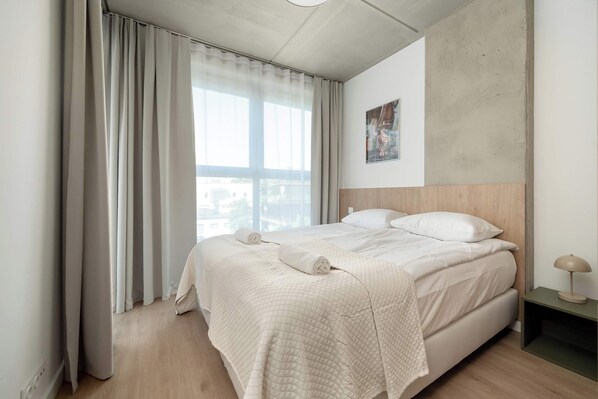 A hotel room with a bed, curtains, a painting, and a nightstand.