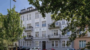 Een meerlaags woongebouw met balkons, geparkeerde auto's en een straatlamp.