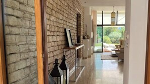 A modern hallway with a stone wall, a wooden floor, and a view into a living area with furniture and a large window. - EXCEPTIONAL VILLA - GOLF - SWIMMING POOL - BREAKFAST AND SERVICES (essaouira)