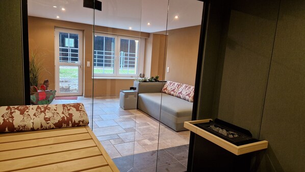 A modern living room with a sofa, a small table, and a fireplace. There are large windows and a door leading outside. - FeWo Rosenberg idyllic property to relax in the countryside (Hillesheim)