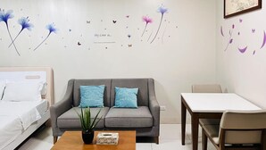 Ein modernes Zimmer mit grauem Sofa, einem kleinen Tisch und einem weißen Bett.