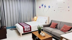 Ein Hotelzimmer mit einem Bett, einem grauen Sofa, einem Holztisch und einer Wand mit floralem Wandbild.