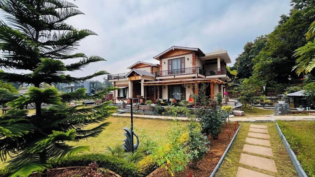 Una casa de dos pisos con un balcón, rodeada por un jardín bien cuidado con diversas plantas y un sendero de piedra.