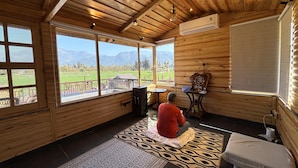 A wooden room with large windows, a ceiling fan, and a prayer mat. - Vanhills : Boutique Stay in Jim Corbett (Kotabagh)