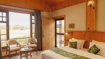 Een kamer met houten lambrisering, een bed, twee stoelen, een tafeltje en een groot raam.