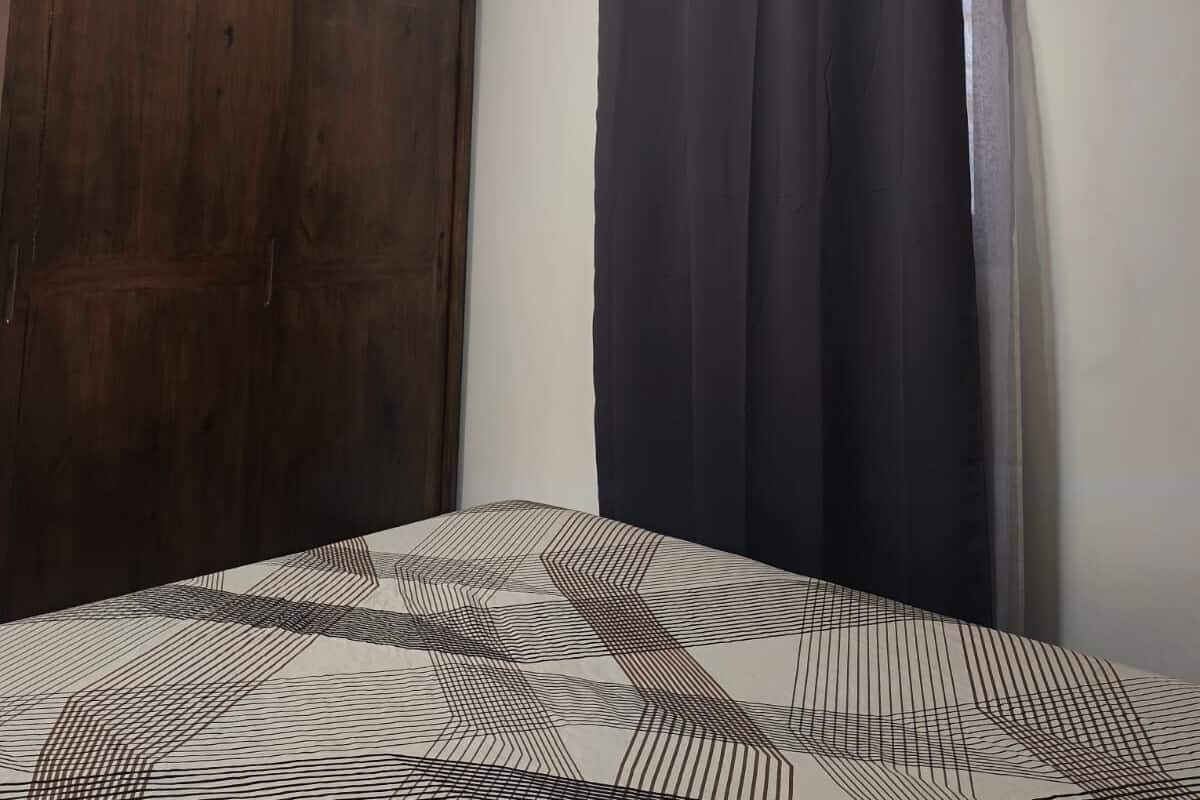 Een slaapkamer met een houten garderobe, een bed met een geborduurd beddegoed, een zwart gordijn en een airconditioning op de muur.
