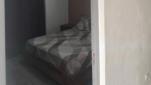 Une chambre à coucher avec un lit, un rideau foncé, une petite table de chevet et un appareil de climatisation fixé au mur.