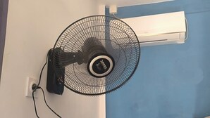 Une chambre d’angle équipée d’un ventilateur sur pied, d’un climatiseur et d’une échelle en métal.