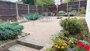 Un jardin à l’arrière de la maison, avec un panier de basket, une corde à linge et un potager où poussent différentes plantes et fleurs.