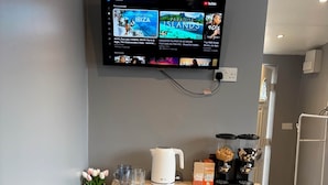 Une petite cuisine équipée d’un four à micro-ondes, d’une machine à café et d’un téléviseur fixé au mur, diffusant un film.