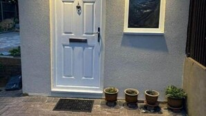 Une maison avec une porte blanche, une petite fenêtre et quatre plantes en pot devant.