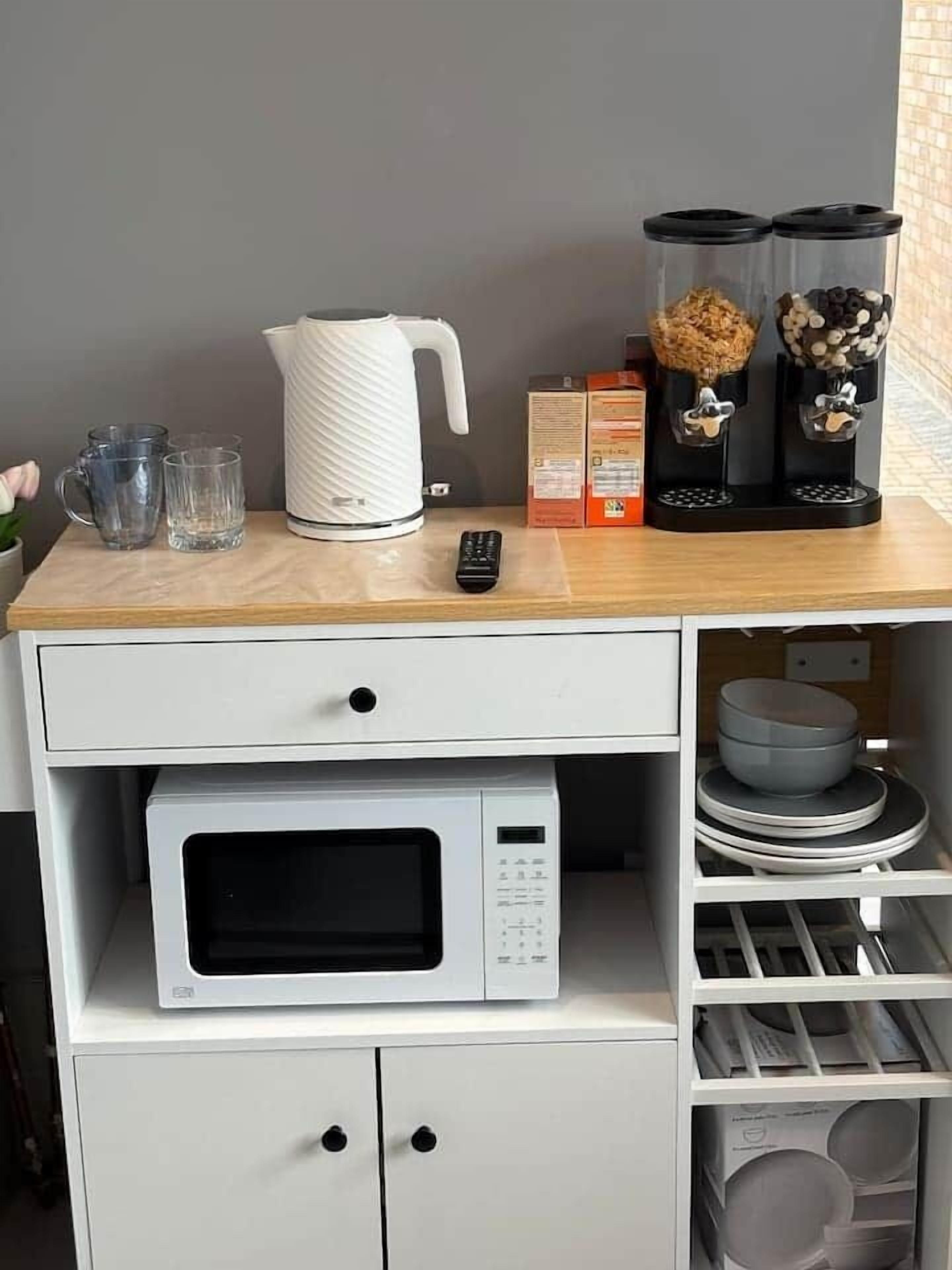 A kitchenette with a microwave, a kettle, a coffee maker, and a remote control on a wooden countertop.
