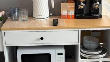 A kitchenette with a microwave, a kettle, a coffee maker, and a remote control on a wooden countertop.