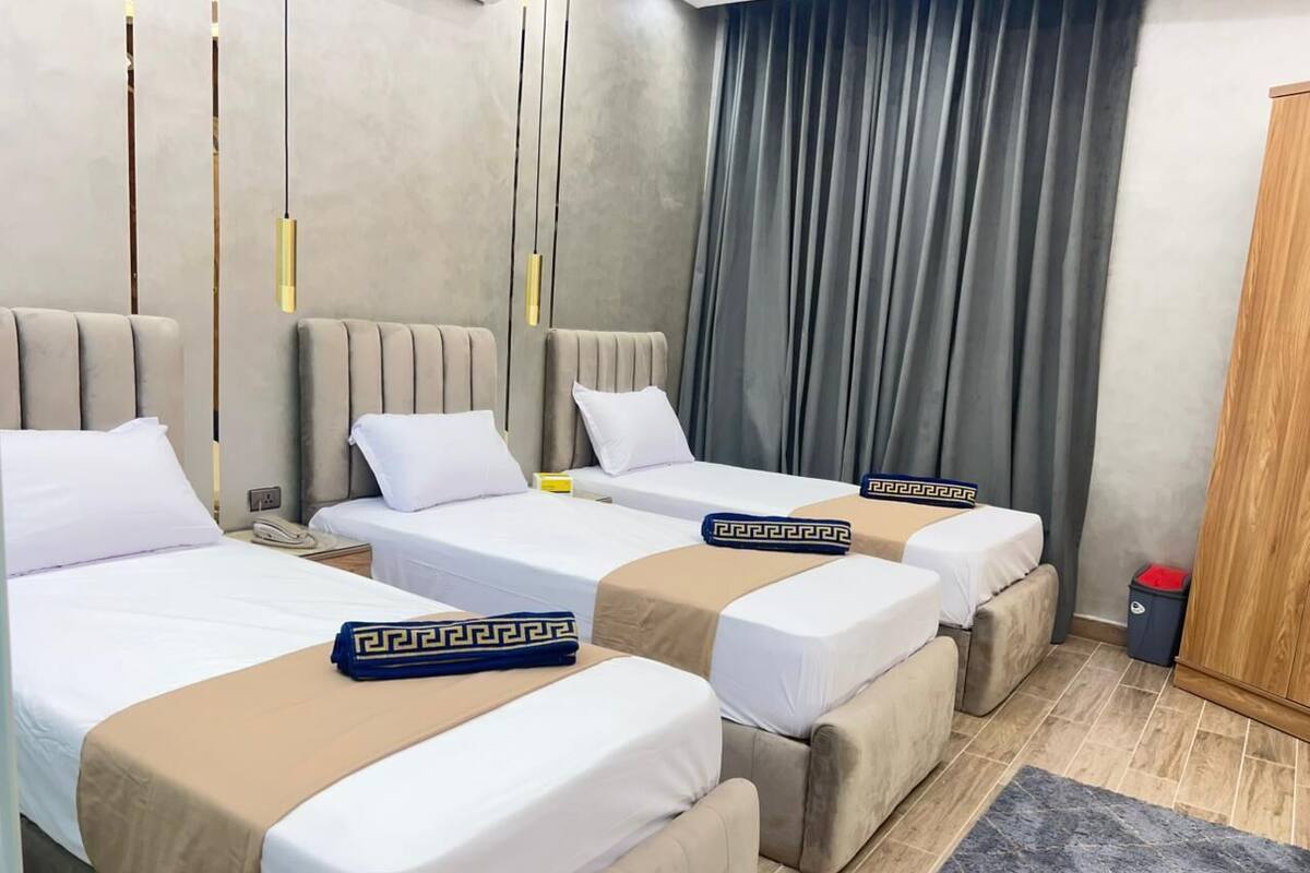 A hotel room with three beds, each with a beige bedspread and a decorative pillow.