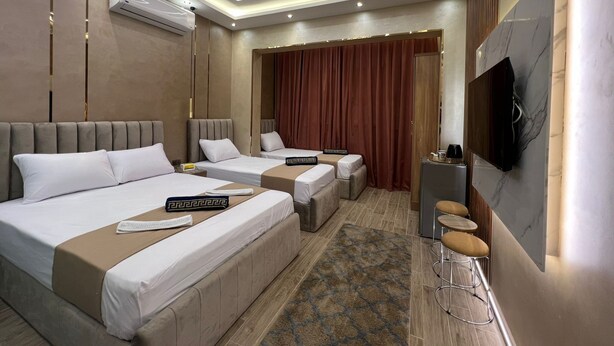 Una camera d'albergo con due letti, una TV, un minibar e un angolo salotto con sgabelli.