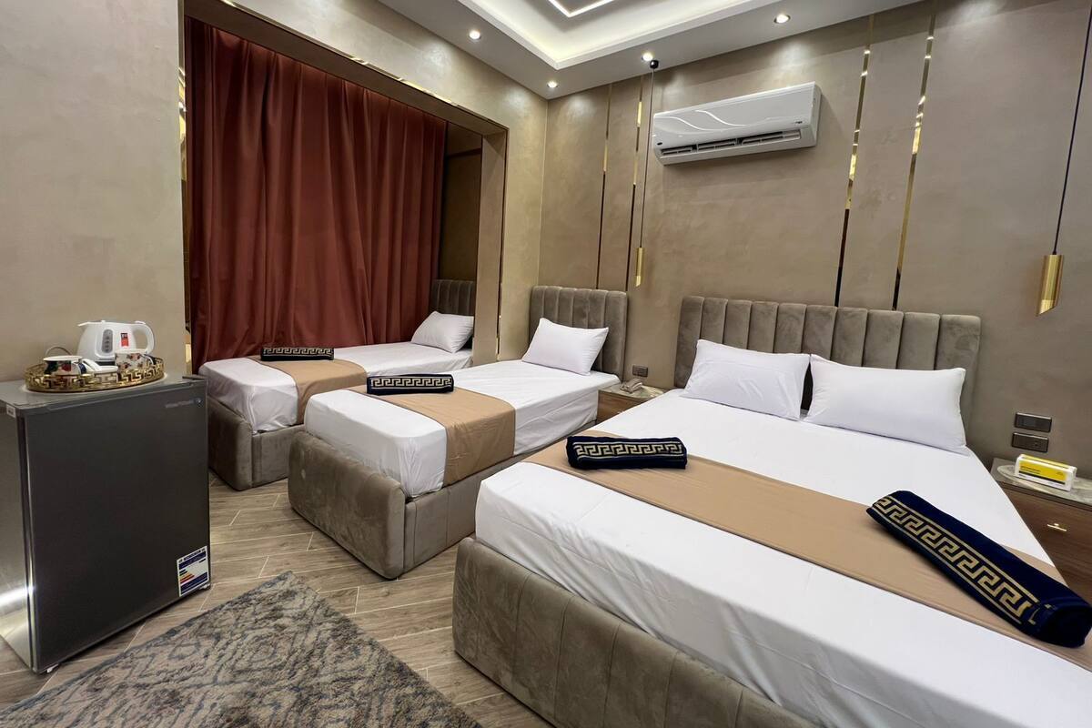 A hotel room with two beds, a minibar, an air conditioning unit, and a modern ceiling design.