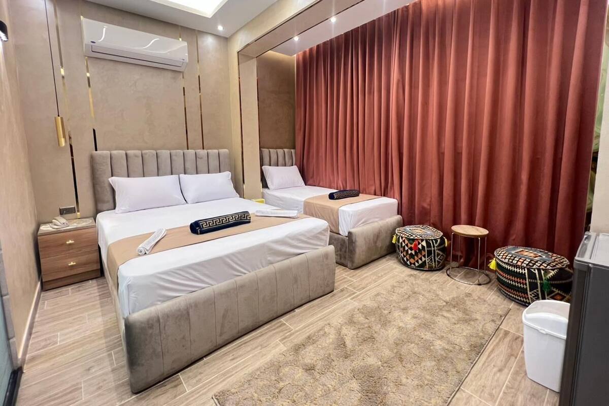 A modern hotel room with two beds, a large mirror, a red curtain, and a small round table.