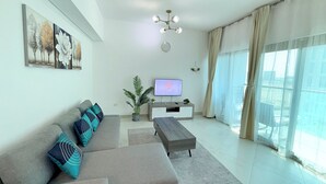 Een moderne woonkamer met een grijze bank, een salontafel, een tv op een meubelstuk, en een groot raam met gordijnen.