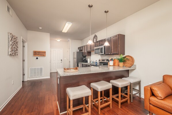 A modern kitchen with a central island, bar stools, and a microwave.