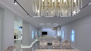 Um quarto luxuoso com uma cama grande, um candelabro, uma televisão e um espaço de estar com uma mesa e cadeiras.