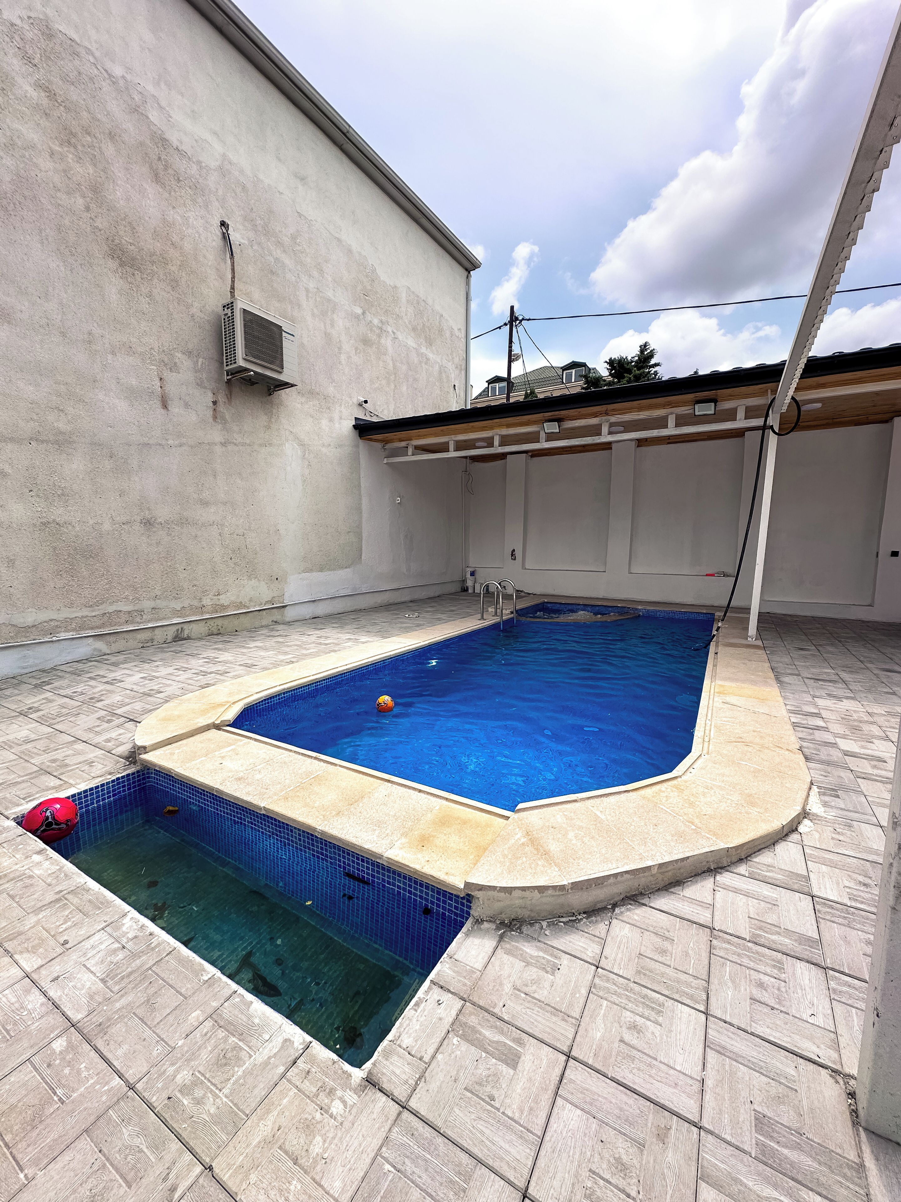 A swimming pool with a tiled deck and a concrete wall.