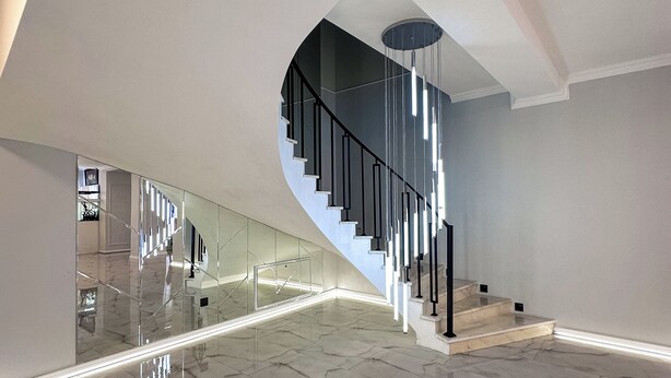 Interior espaçoso e moderno com escadaria curva, piso de mármore e guarda-corpo de vidro.