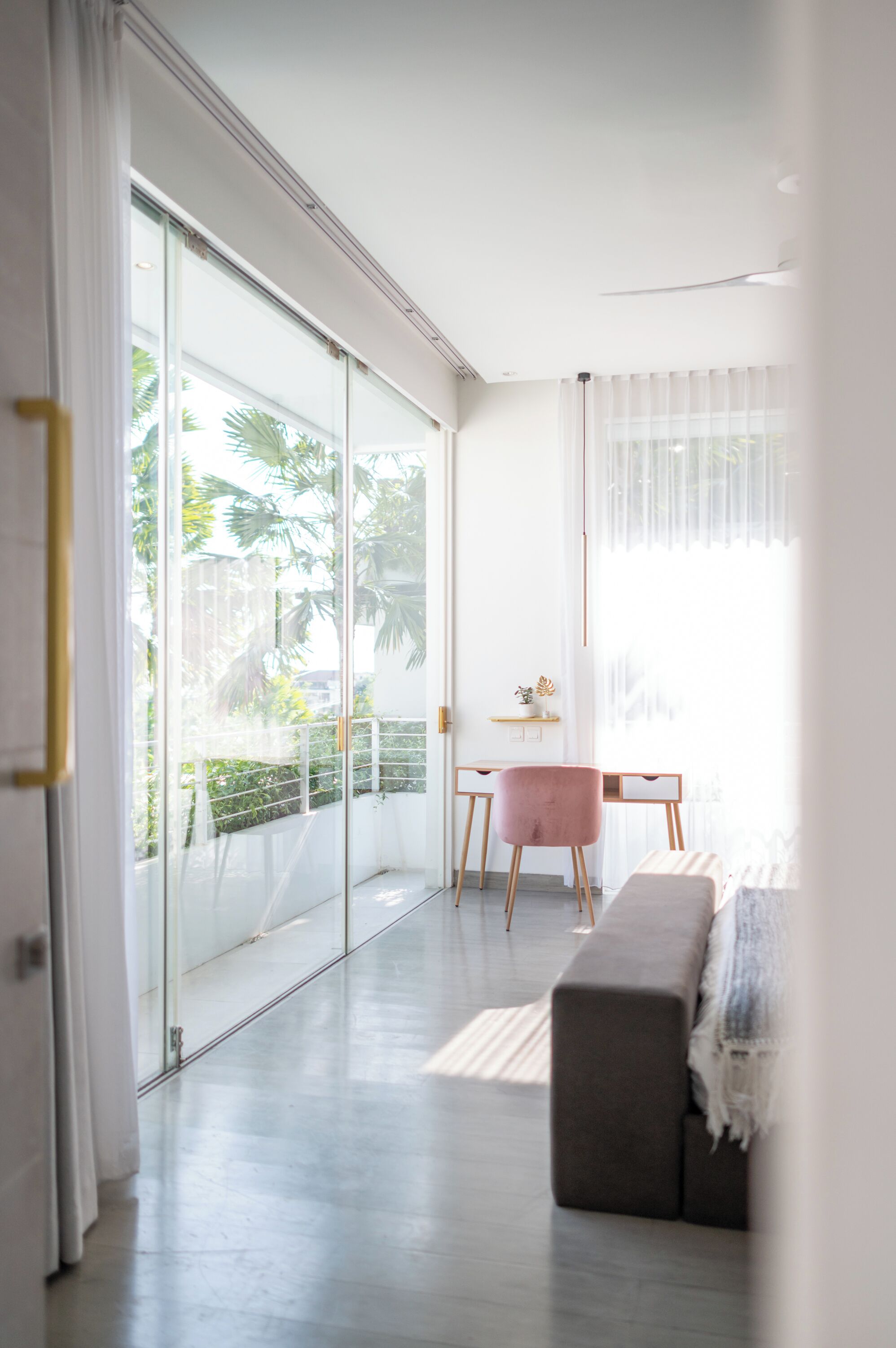 Ein modernes Wohnzimmer mit einer Schiebeglastür, die auf einen Balkon führt, einem rosa Sessel, einem kleinen Tisch und einer Bank.