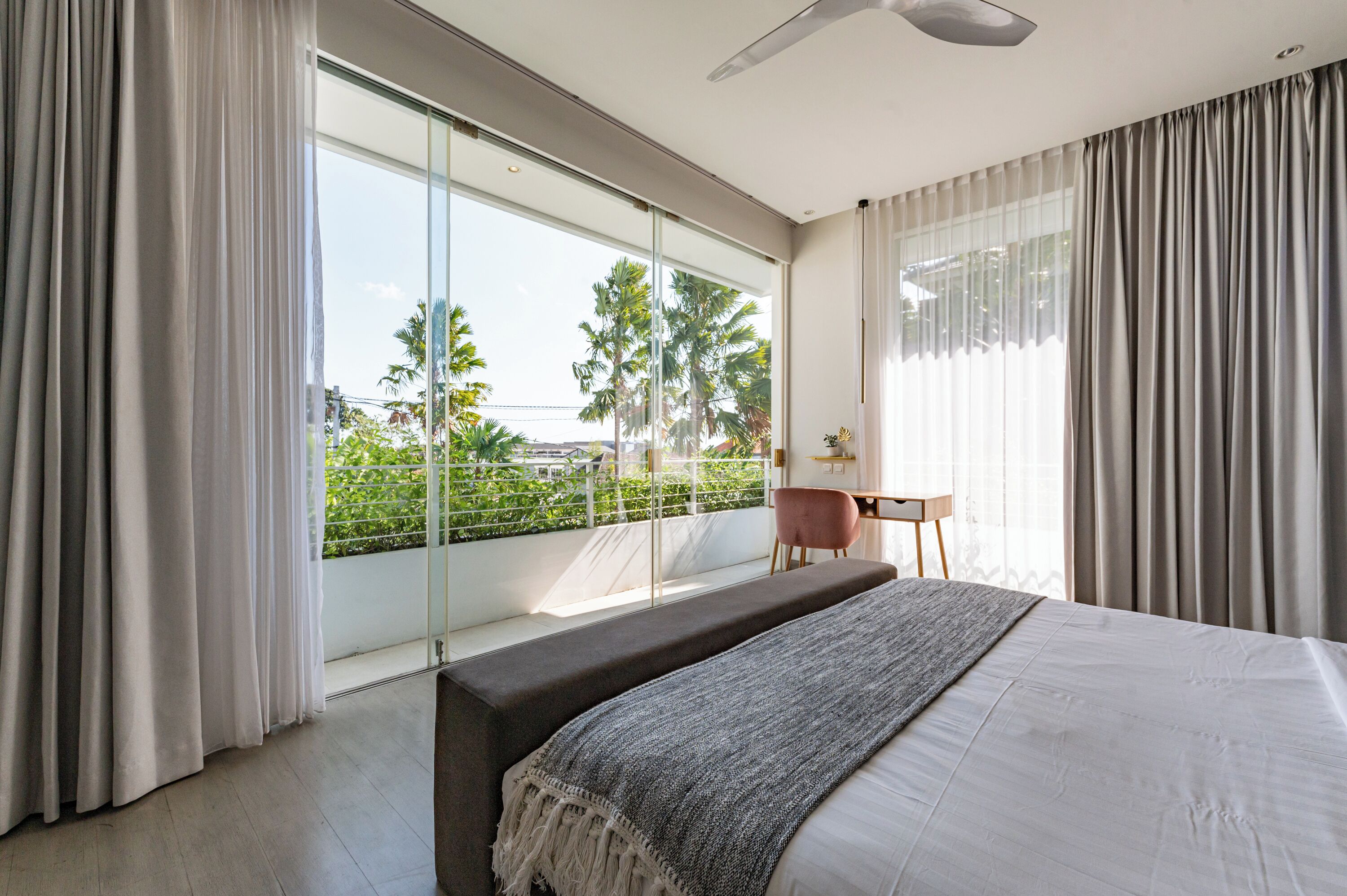 A modern bedroom with a large bed, a desk, and a view of greenery outside.
