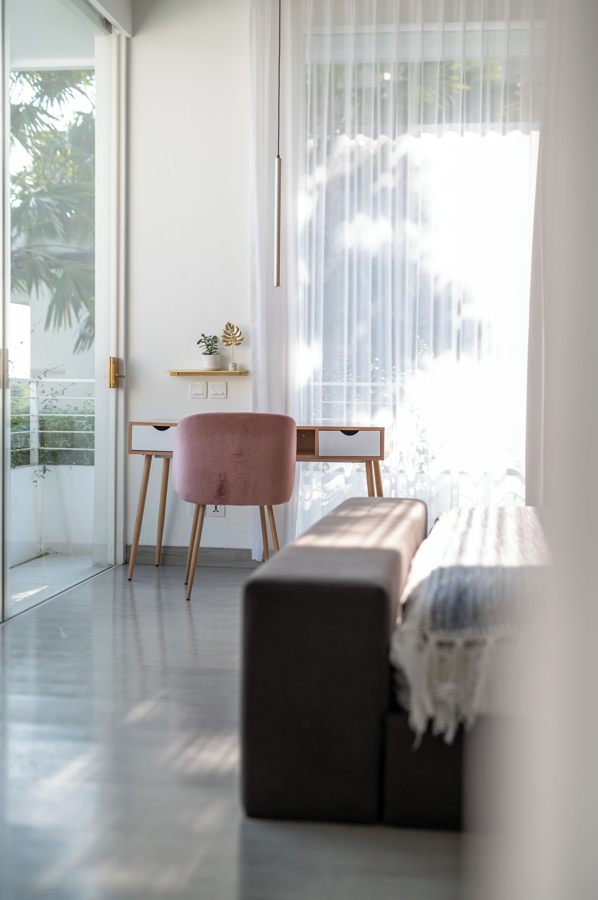 A modern room with a large window, a pink chair, a wooden desk, and a bench.