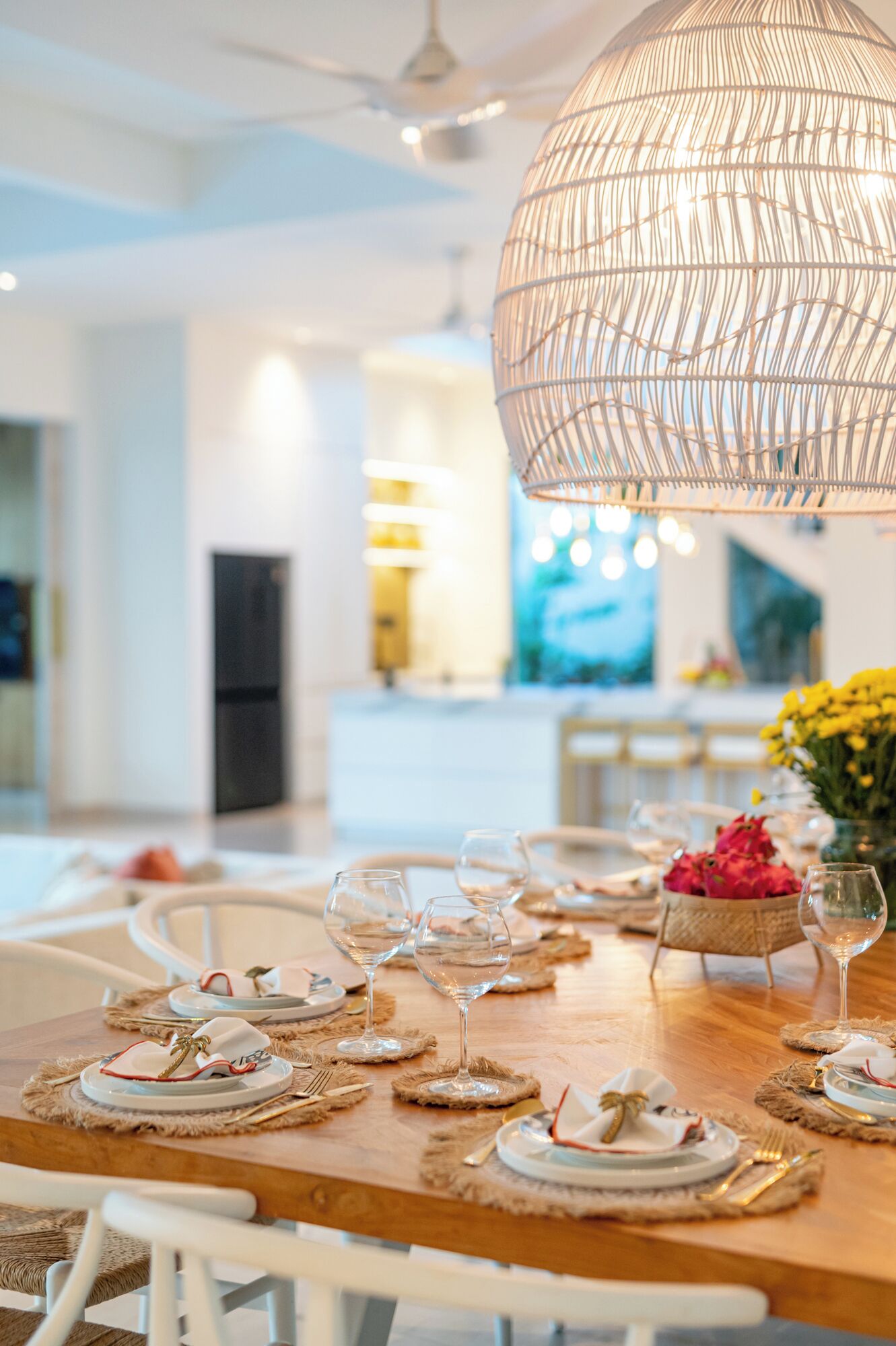 Un comedor con una mesa de madera dispuesta para una comida, una lámpara colgante y una cocina al fondo.