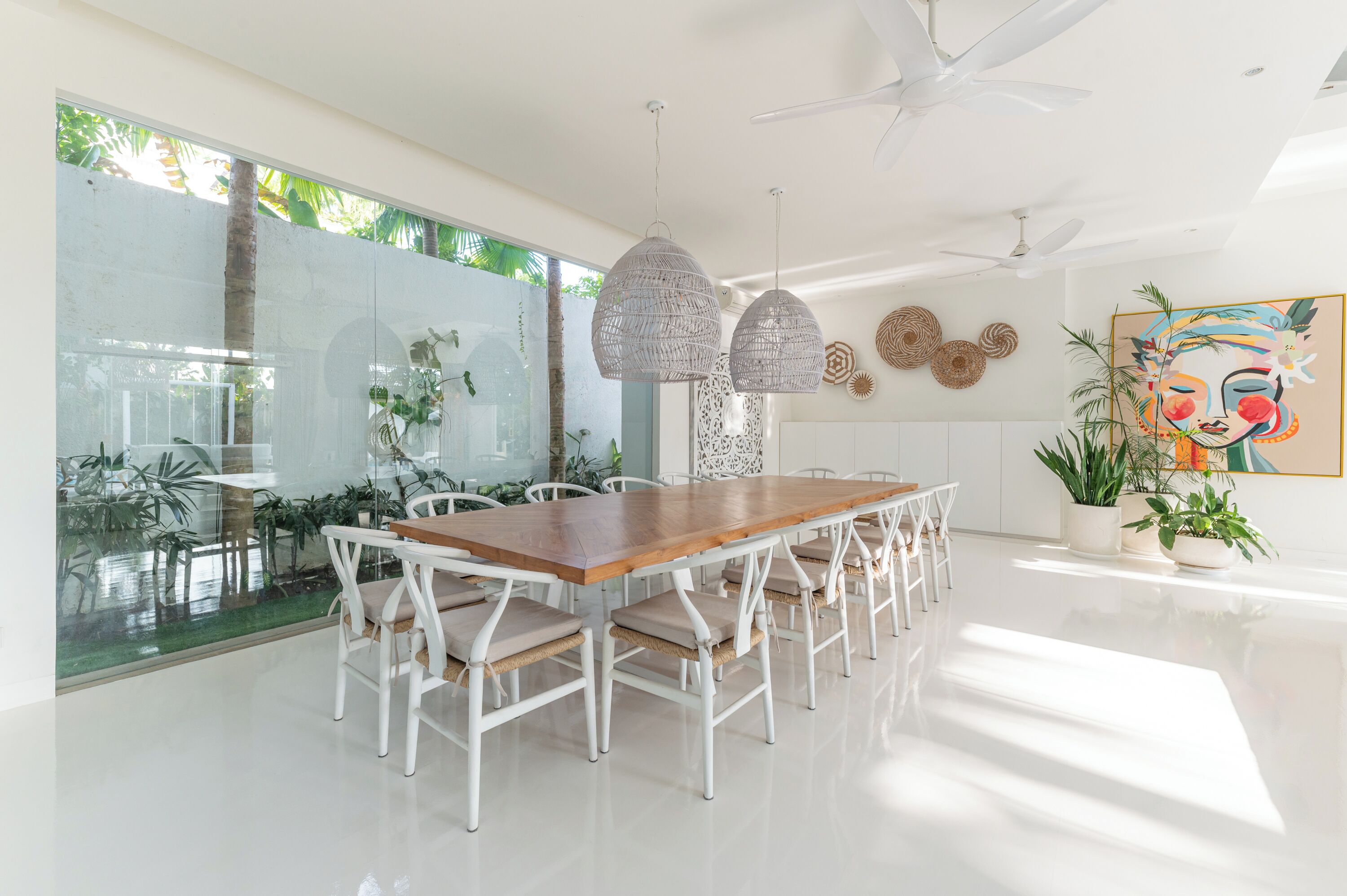 A modern dining area with a wooden table and white chairs, large windows, and ceiling fans.