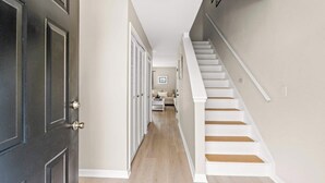 A hallway with a dark door, a staircase, and a living area with a sofa and coffee table.